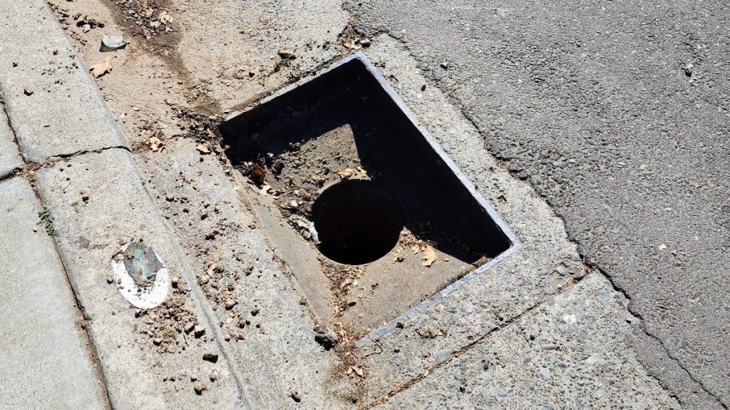 An image of a curbside storm drain without a grate cover.